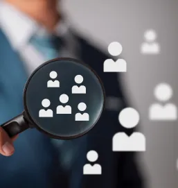 A magnifying glass with tiny employee emojis floating around it. In the background, a man in business attire is holding the same magnifying glass. This image represents the ease of finding a job in Dubai through online platforms. The magnifying glass represents the search for jobs, and the employee emojis represent the many opportunities available. The man in business attire represents the success of those who have found jobs in Dubai.