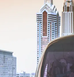 Side view of a metro train passing in front of tall modern buildings.